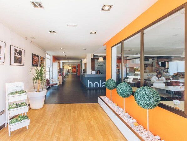A modern hotel lobby with a reception desk, seating area, and a view into the dining area.
