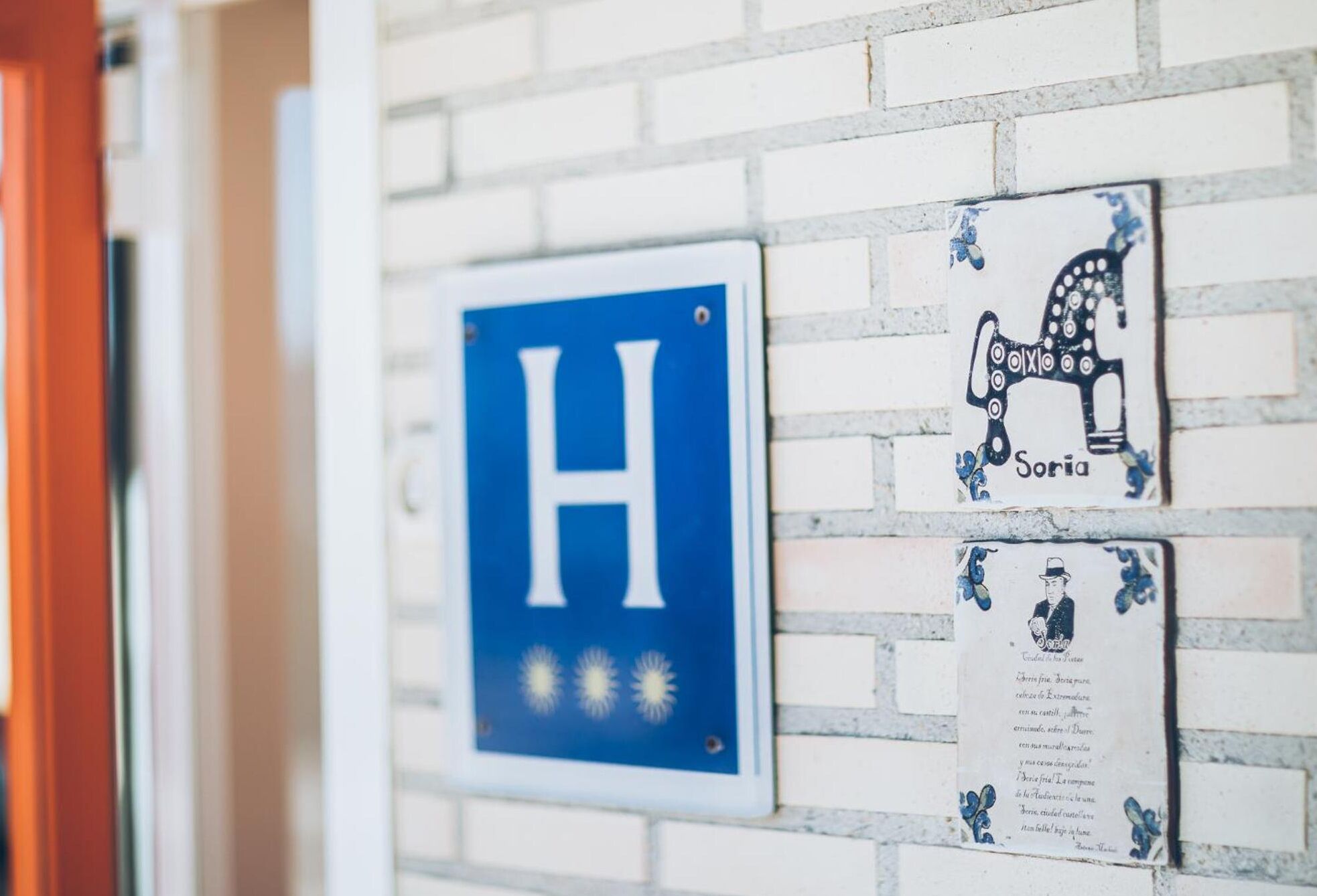 Un letrero azul con una 'H' blanca que indica un hospital, y una placa decorativa con un caballo y el nombre 'Soria'.