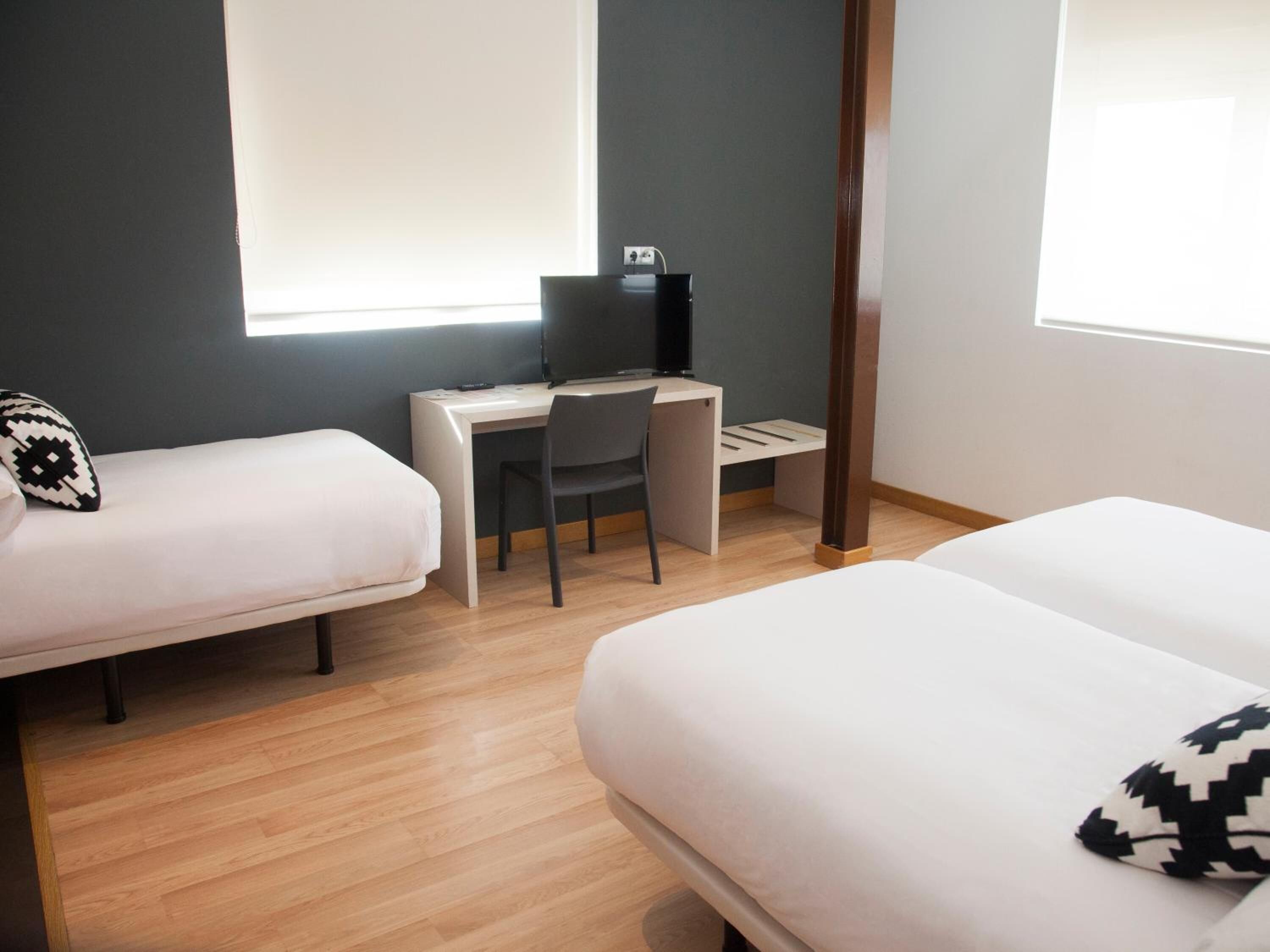 Ein Hotelzimmer mit zwei Einzelbetten, einem Schreibtisch mit Stuhl und einem großen Fenster.