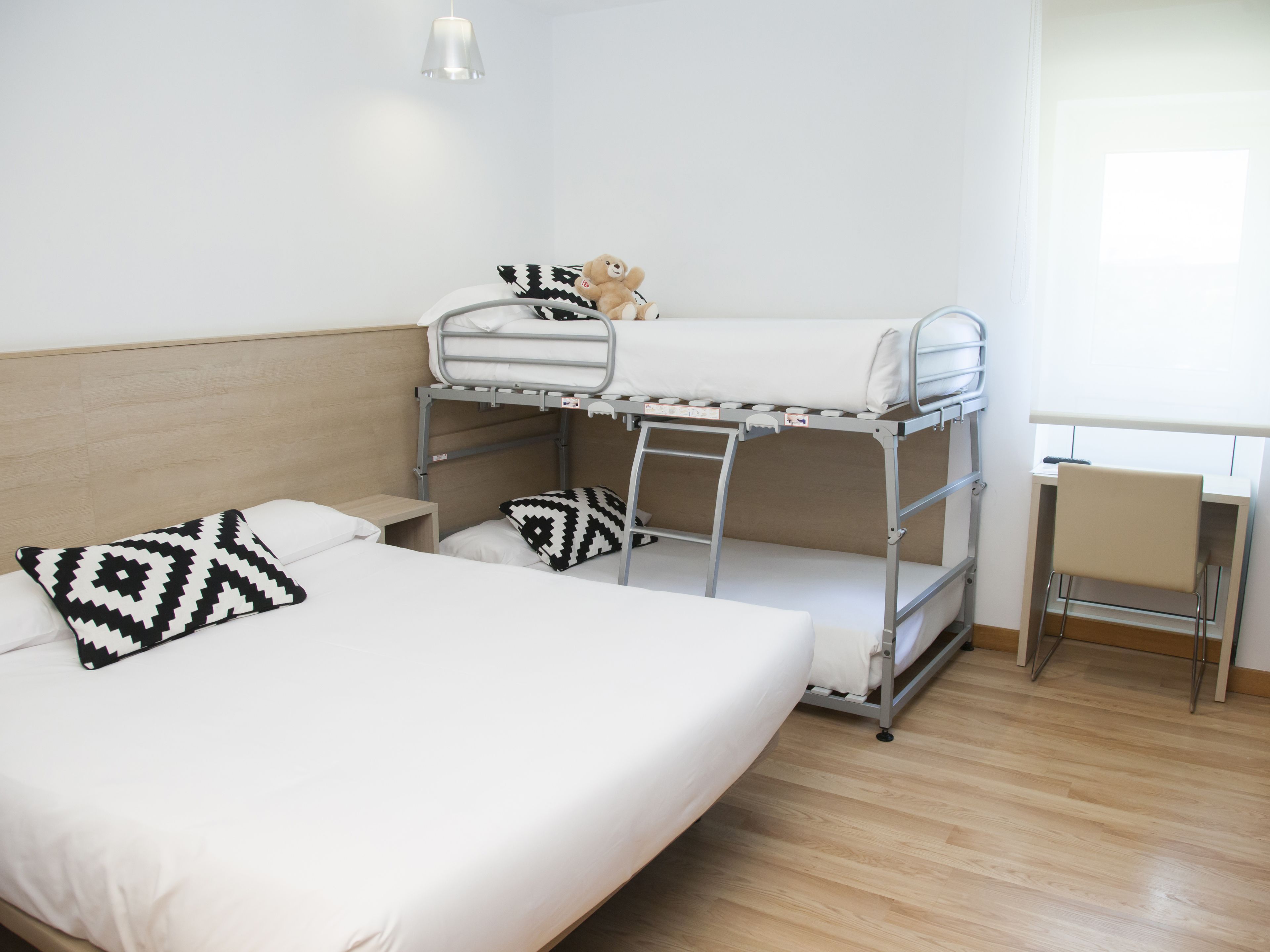 A bunk bed room with a desk and chair, a teddy bear on the top bunk, and patterned pillows.