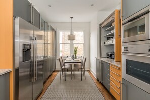 A modern kitchen with stainless steel appliances, a dining table with chairs, and a patterned rug. - Eson2 - Charming 3 Bedroom Flat in Chelsea (London)