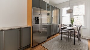 A modern kitchen with a stainless steel refrigerator, grey cabinets, and a dining area with a table and chairs. - Eson2 - Charming 3 Bedroom Flat in Chelsea (London)