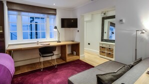 A modern bedroom with a wooden desk, a black chair, a TV, a mirror, and a red carpet. - Eson2 - The York Street Nest (London)