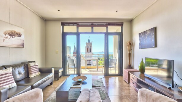 A living room with a sofa, coffee table, and TV, with a balcony and city view. - Atlantic Views 5 (Cape Town)