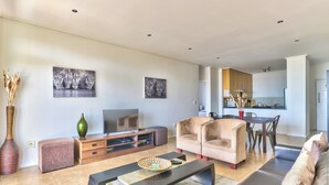 A modern living room with a sofa, coffee table, and TV. A kitchen is visible in the background. - Atlantic Views 5 (Cape Town)