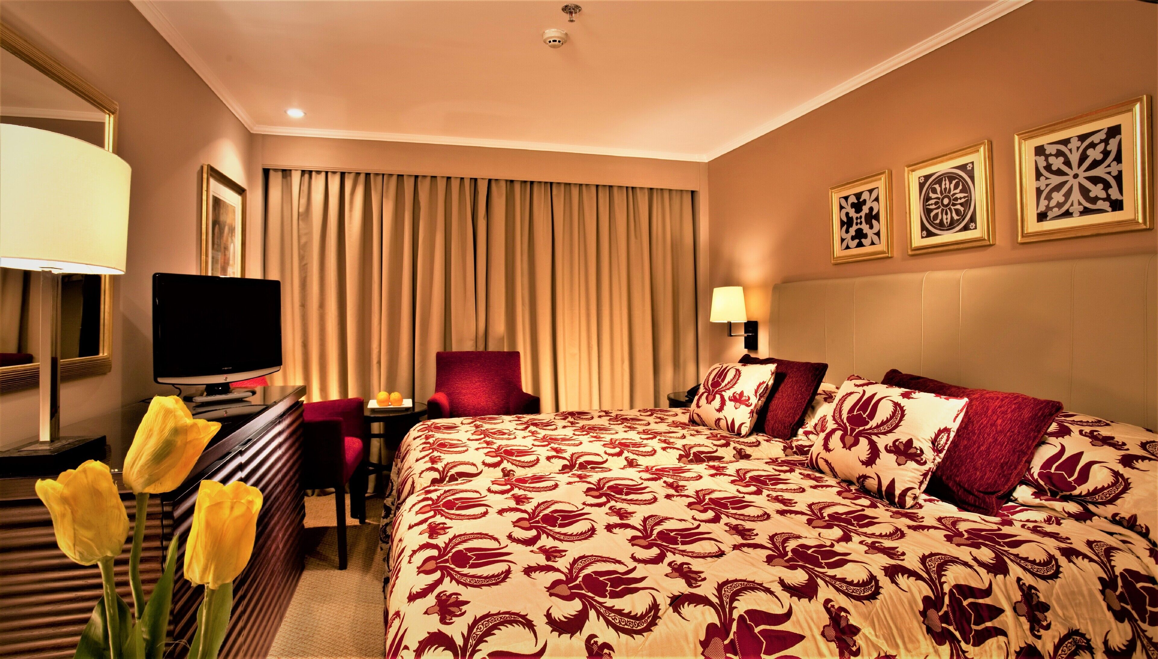 A hotel room with a large bed, a desk with a television, a chair, a lamp, and a window with curtains.