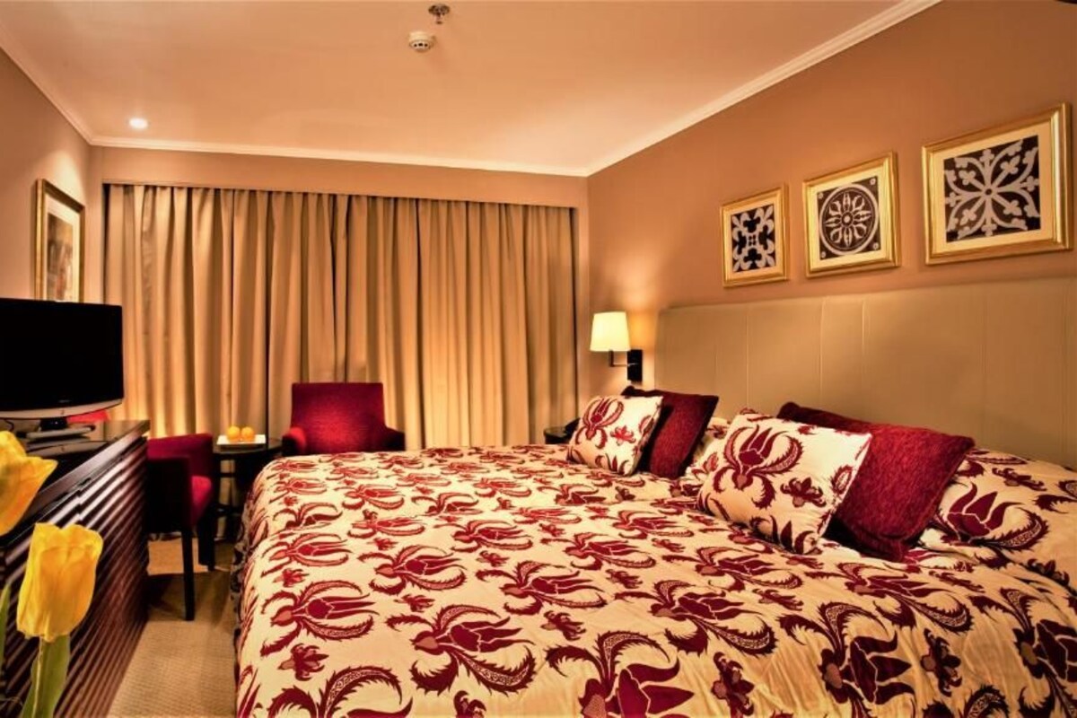 Habitación de hotel con una cama grande, un escritorio con televisor, una silla y una ventana con cortinas.