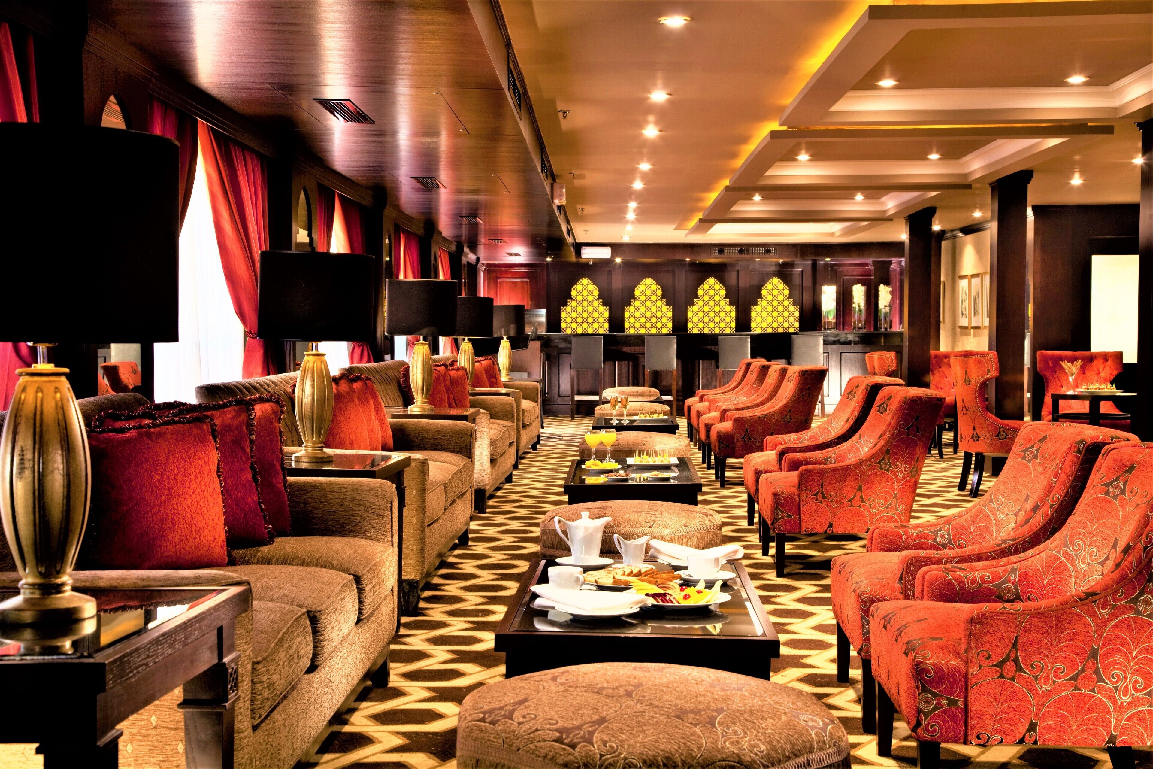 Eine luxuriöse Hotellobby mit bequemen Sitzgelegenheiten, einem zentralen Couchtisch mit Frühstücksangeboten und einem gemusterten Teppich.