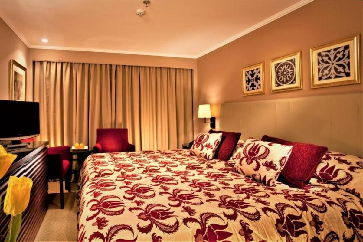 A hotel room with a large bed, a desk with a TV, a chair, and a window with curtains.