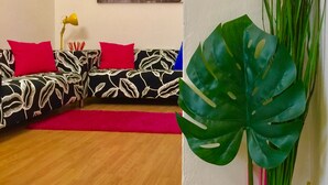 Sala de estar com sofá em formato de L, tapete vermelho e uma planta grande.