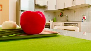 Uma cozinha com armários brancos, bancada verde e uma maçã vermelha em tábua de corte.