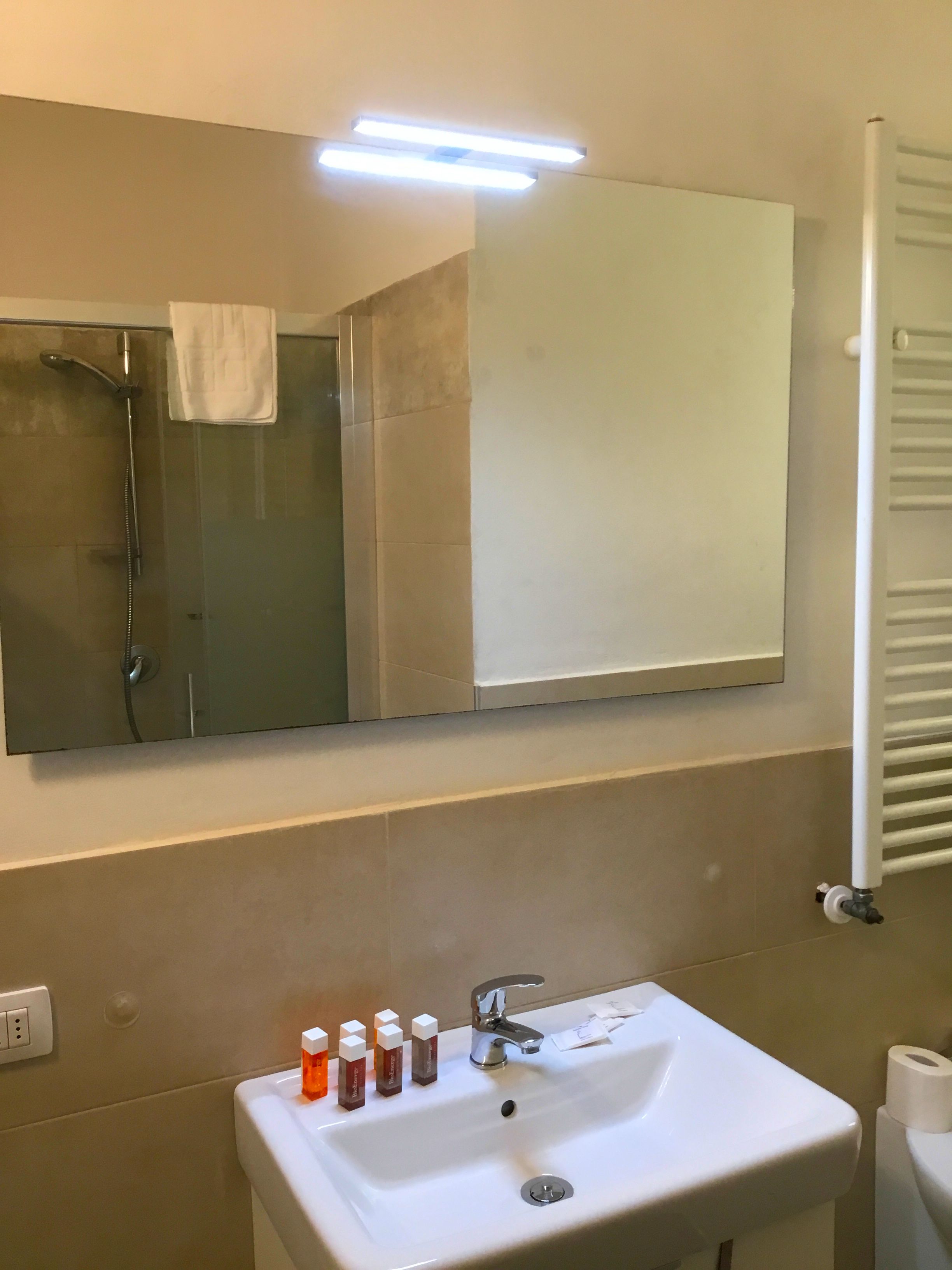 A bathroom with a white sink, a mirror, and a shower. There are toiletries on the sink.