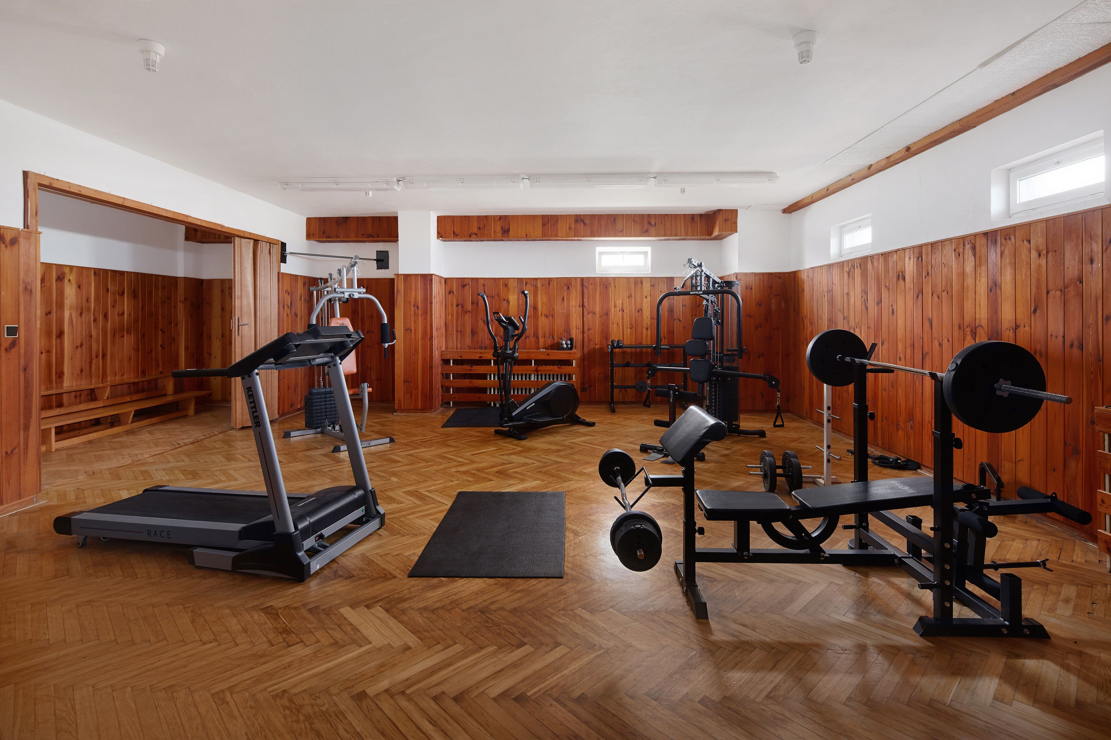 A gym with wooden walls, a treadmill, weight benches, and various exercise equipment.