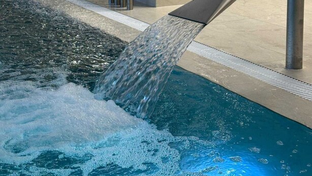 An indoor pool with a water feature, a stone wall, and a potted plant. - Hotel Červenohorské sedlo (Loucna nad Desnou)