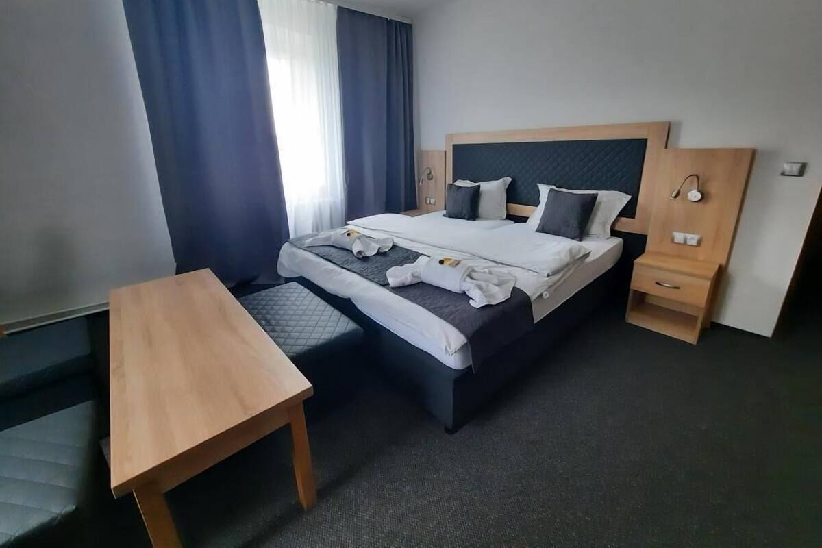 A hotel room with a bed, bedside tables, a desk, and a window with curtains.