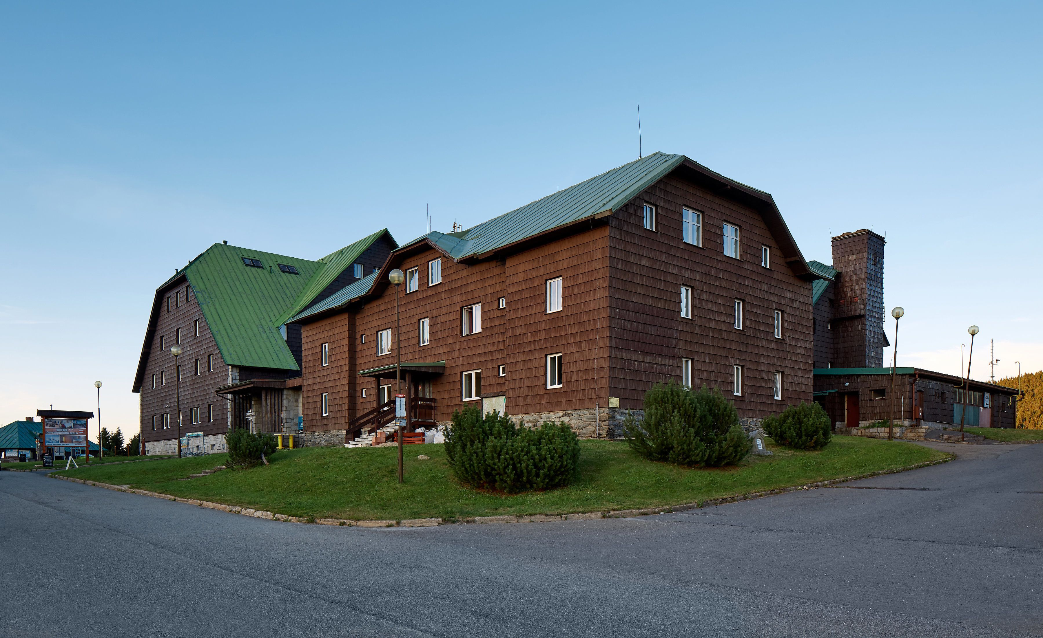 A large, multi-story building with a green roof, multiple windows, and a stone base.
