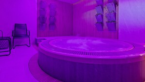 A modern spa room with a circular hot tub, vertical garden panels, and a black chair. - Hotel Červenohorské sedlo (Loucna nad Desnou)