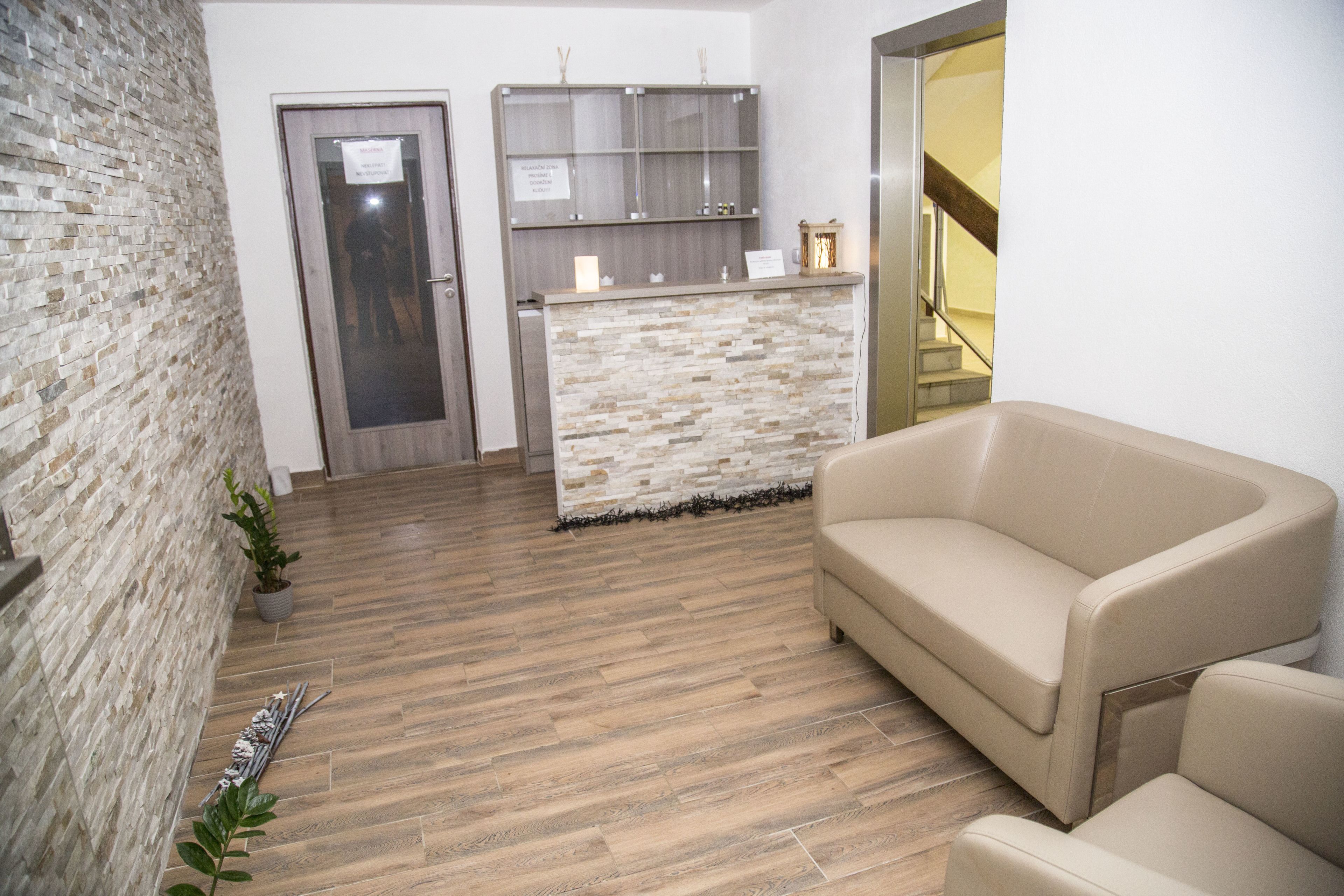 A reception area with a stone wall, a reception desk, a beige sofa, and a staircase in the background.