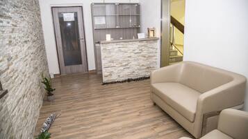 A reception area with a stone wall, a reception desk, a beige sofa, and a staircase in the background.