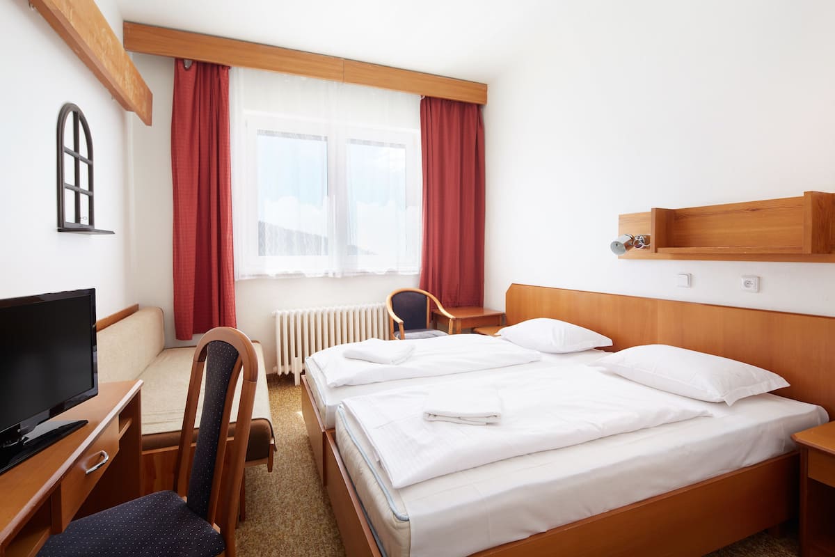 A hotel room with a bed, a desk with a television, a chair, and a window with curtains.