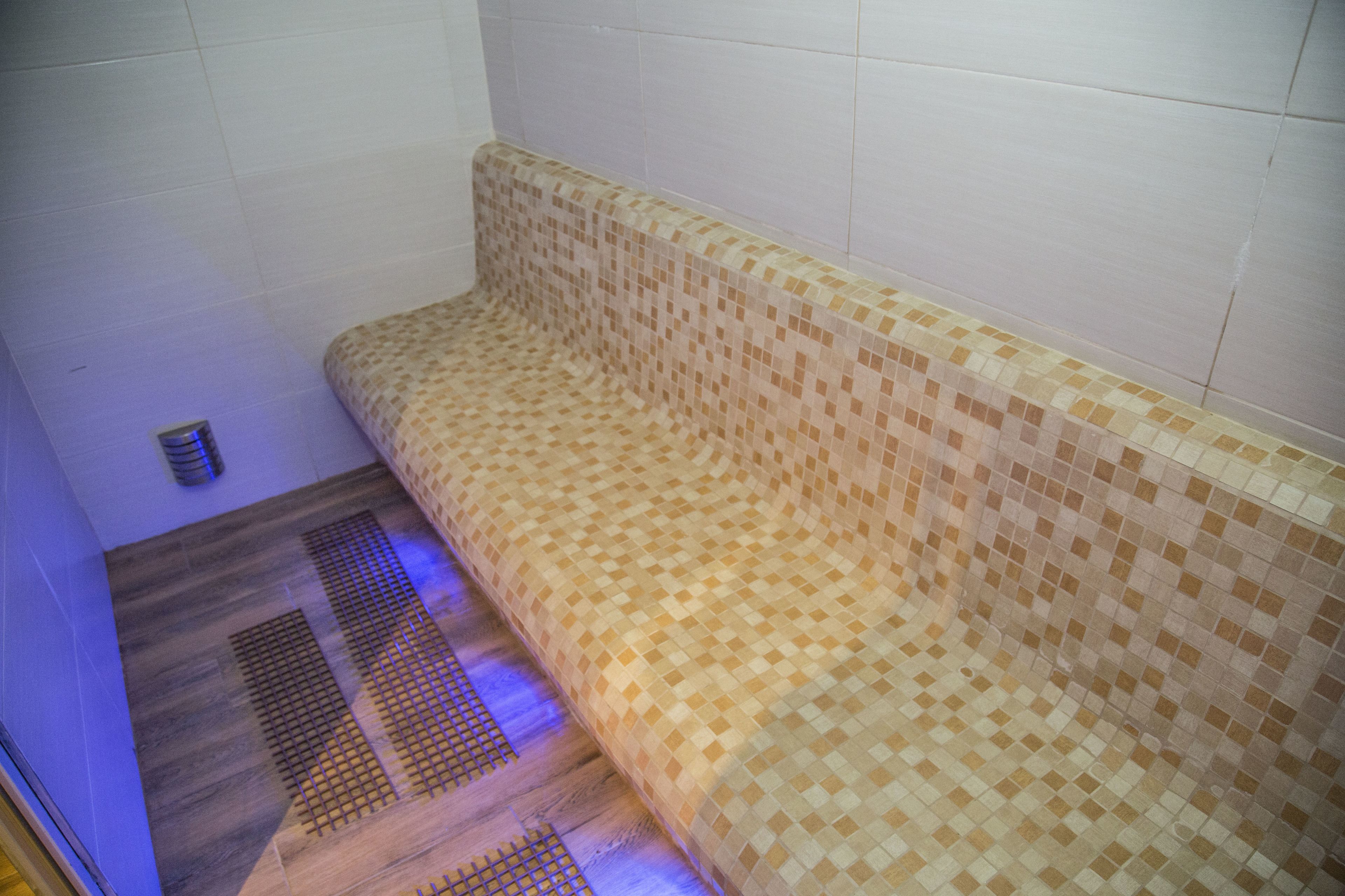 A tiled bench with a checkered pattern, a vent on the floor, and a tiled wall.