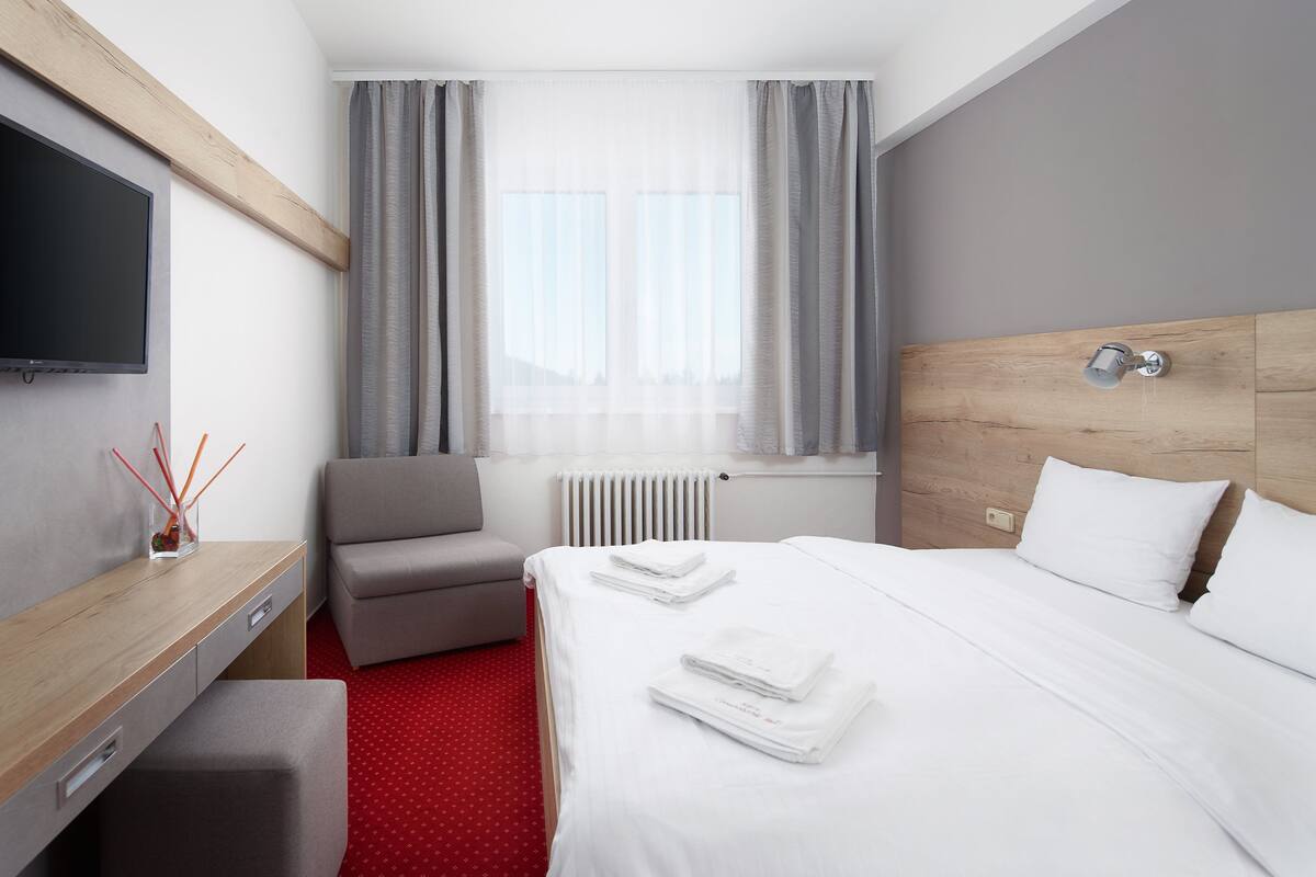 A hotel room with a bed, a desk, a chair, a TV, and a window with curtains.