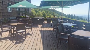 An outdoor patio with wooden deck, tables, chairs, and green umbrellas labeled 'Pilsner Urquell'. - Hotel Červenohorské sedlo (Loucna nad Desnou)