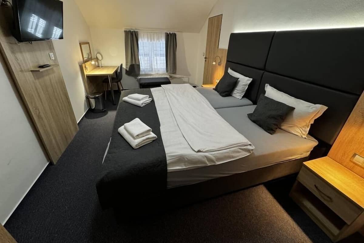 A hotel room with a large bed, a desk, a chair, a TV, and a window with curtains.