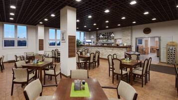 Un comedor espacioso con varias mesas y sillas, una zona de bar con pared de piedra y grandes ventanales que permiten la entrada de luz natural.