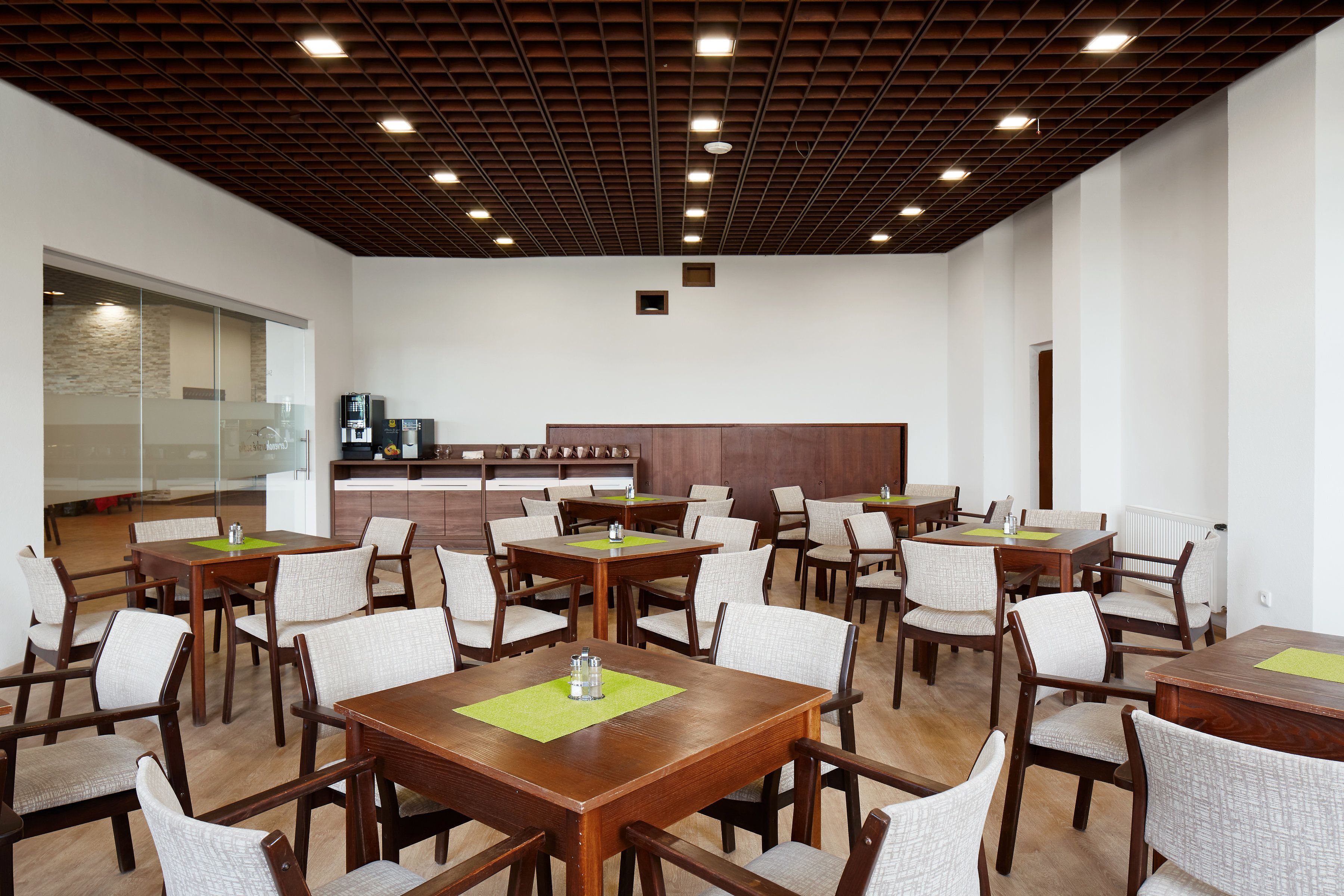 Un comedor amplio con varias mesas y sillas de madera, una cocina al fondo y un diseño de techo moderno.