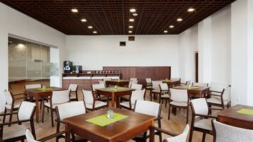 Un comedor amplio con varias mesas y sillas de madera, una cocina al fondo y un diseño de techo moderno.