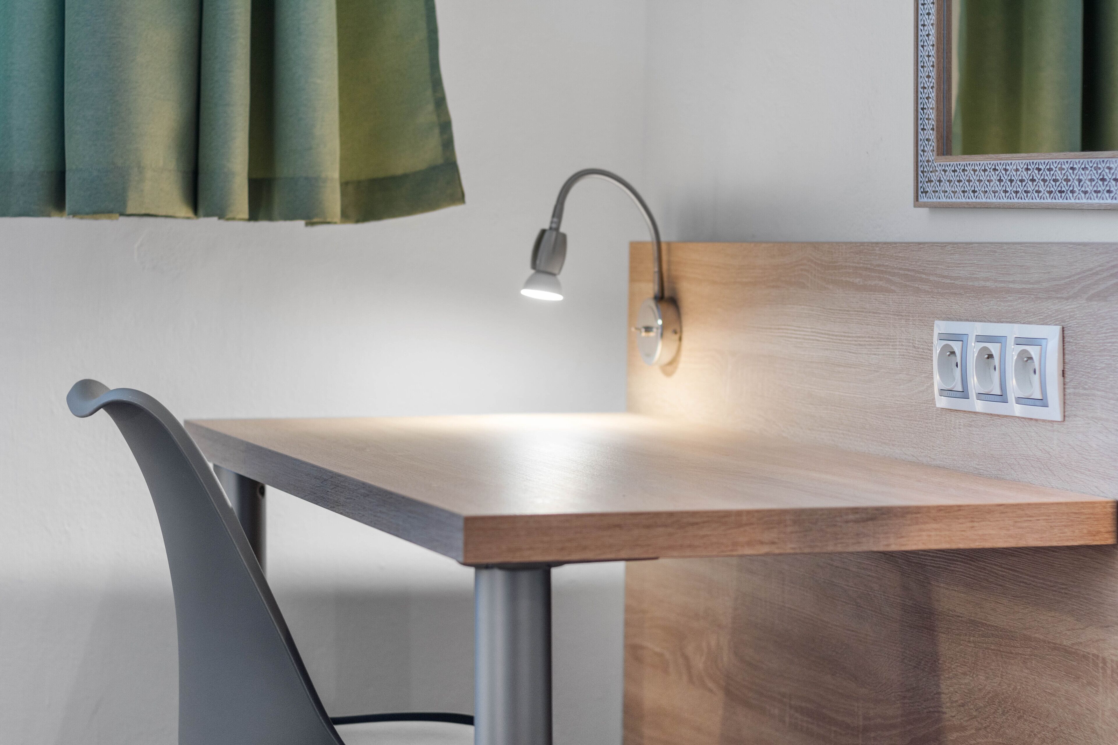 A modern desk with a wooden finish, a metallic chair, and a wall-mounted lamp.