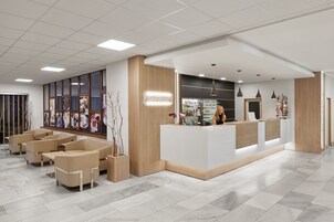Un área de recepción moderna con un mostrador blanco, asientos color beige y un amplio ventanal que exhibe obras de arte.