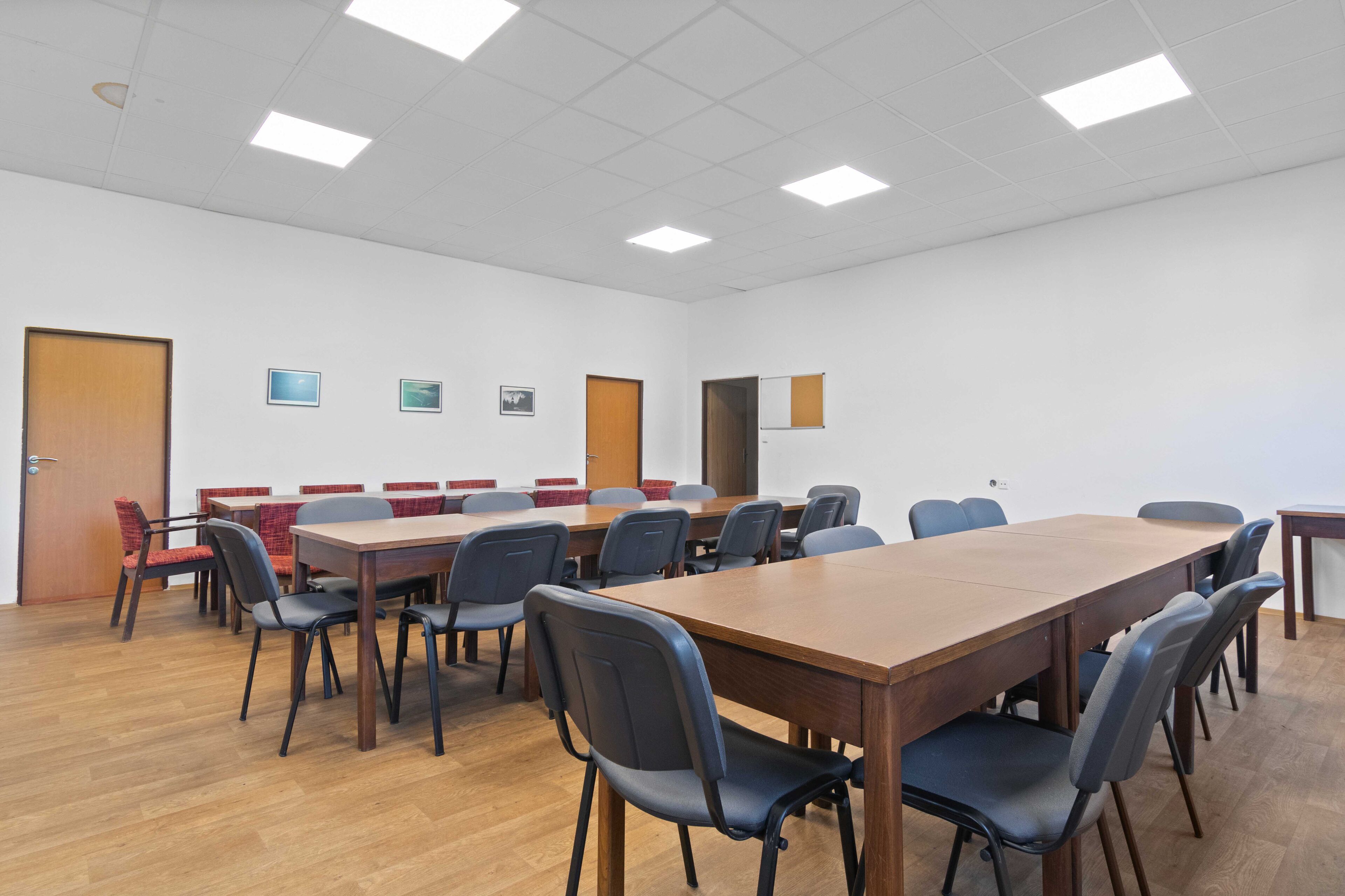 Une salle de conférence avec une longue table en bois, de nombreuses chaises et un tableau blanc au mur.