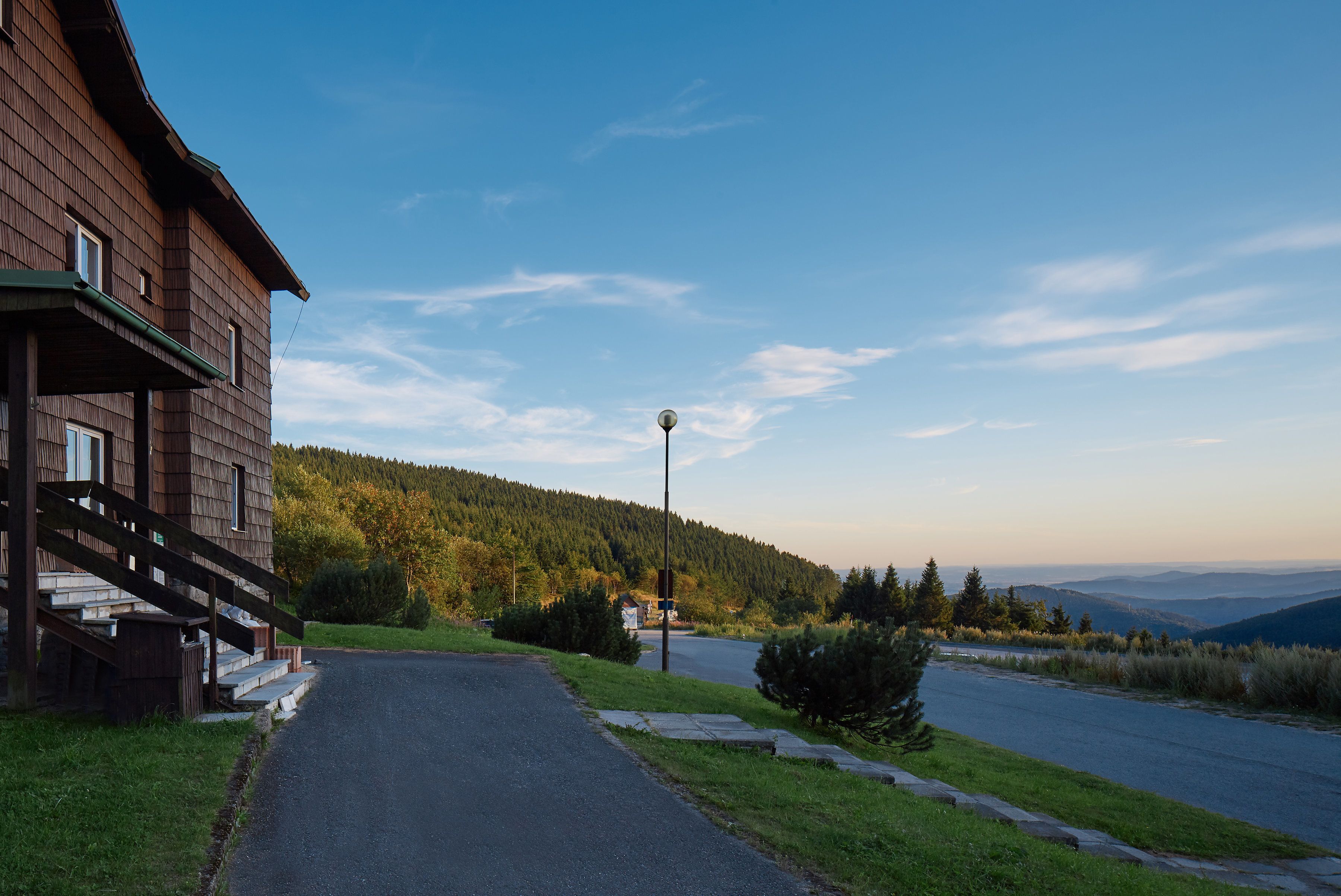 A wooden cabin with a porch and a paved driveway leading to a road.