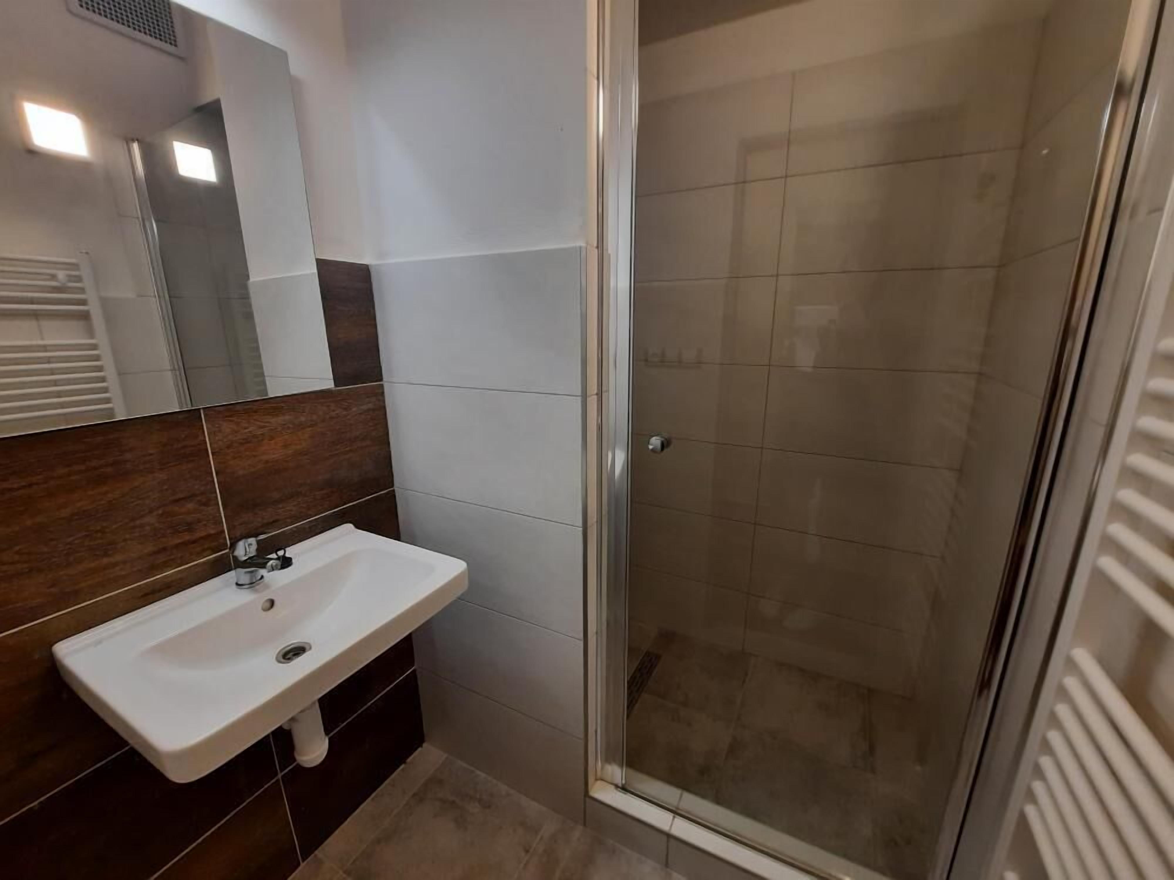 Et moderne badeværelse med en hvid vask, mørk træpanelfacade og et glasbadeværelsesafskærmning.