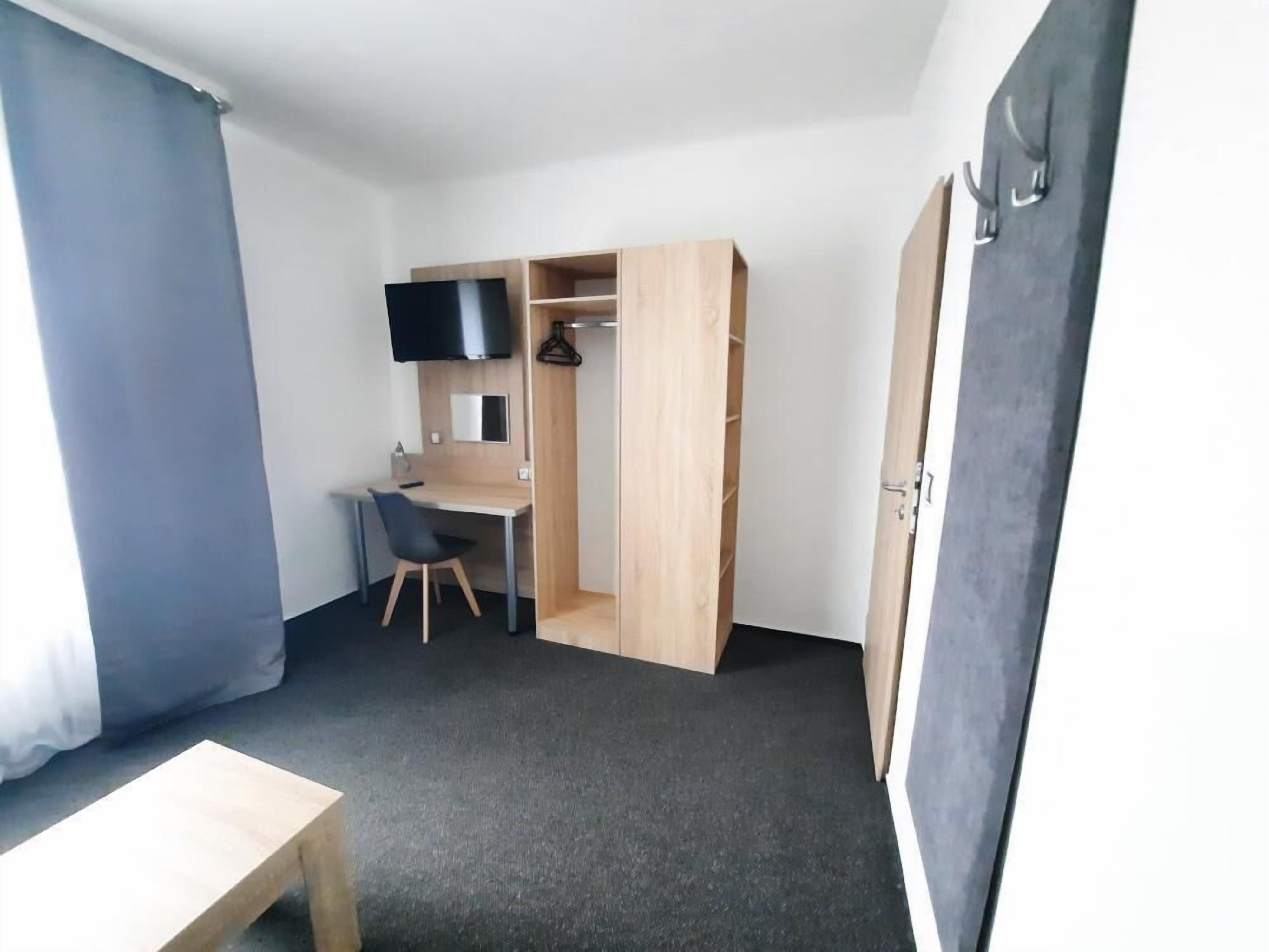 Habitació compacta amb escriptori, cadira i televisió penjada a la paret.