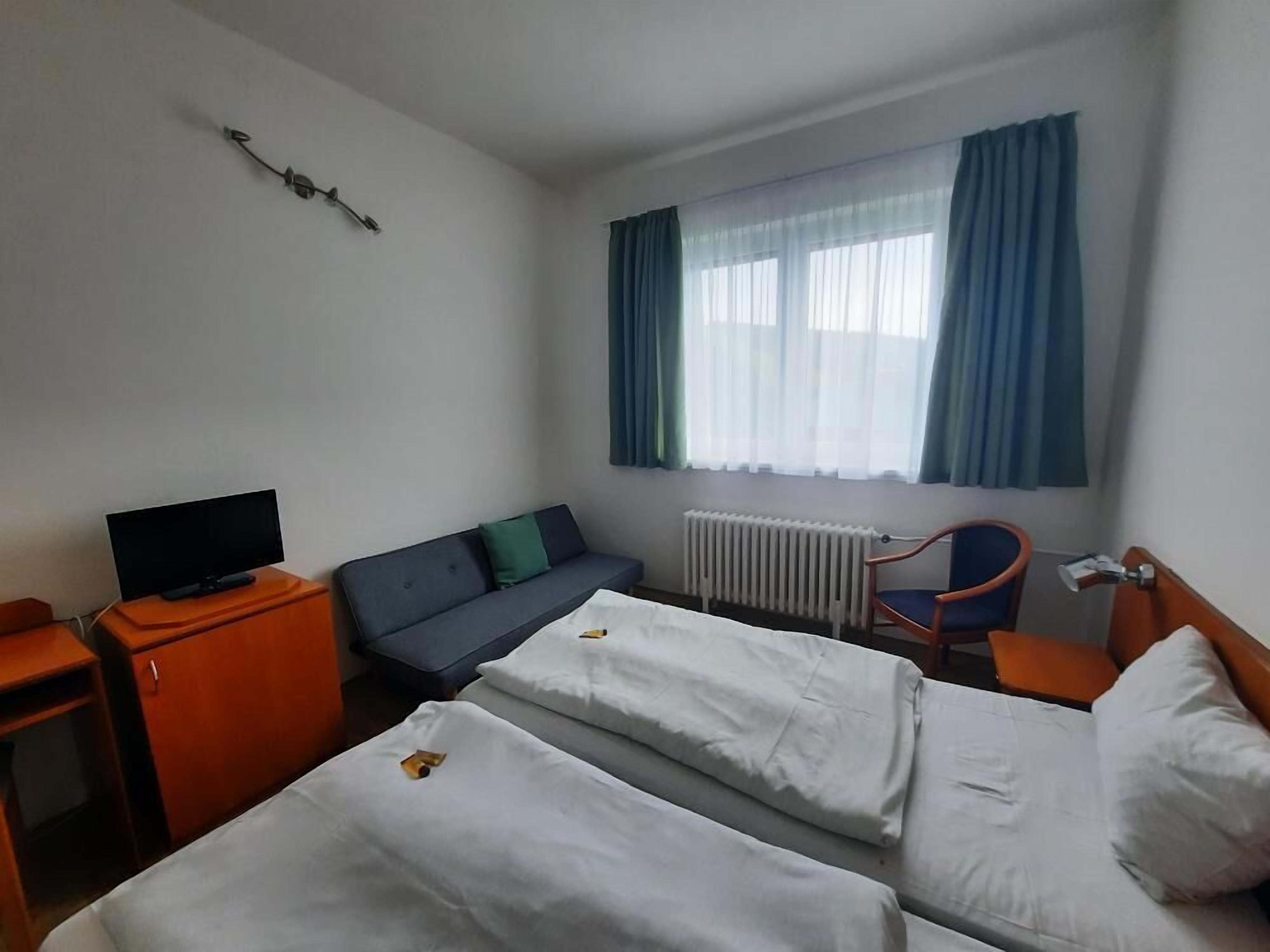 Habitación de hotel con dos camas, televisión, sofá, sillón y ventana con cortinas.