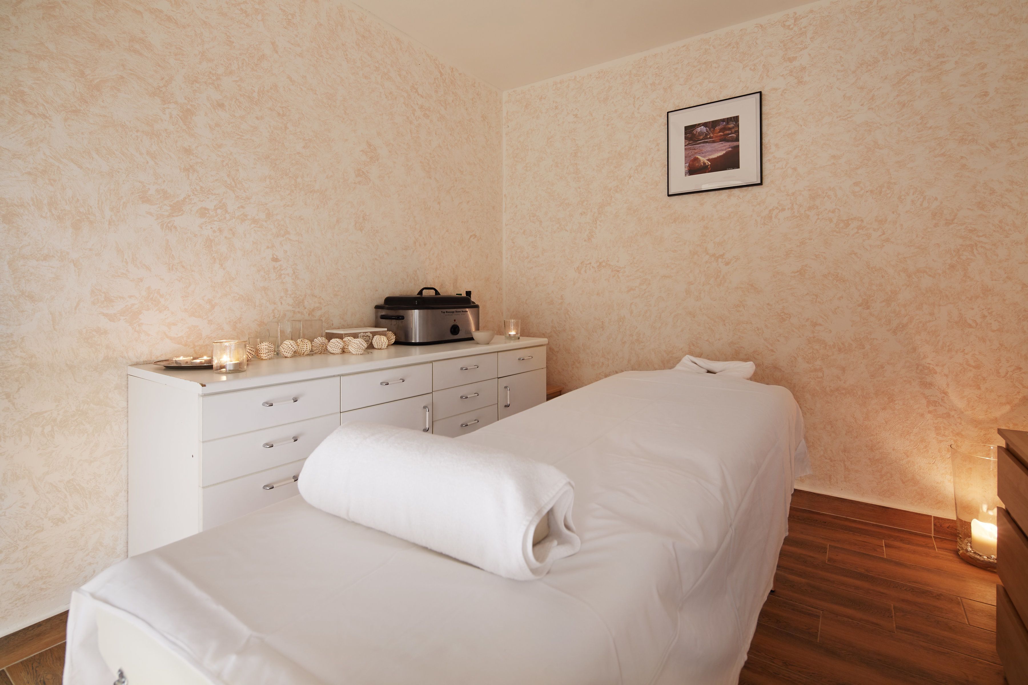 A bedroom with a bed, a dresser, a wall-mounted picture, and a lit candle on the floor.