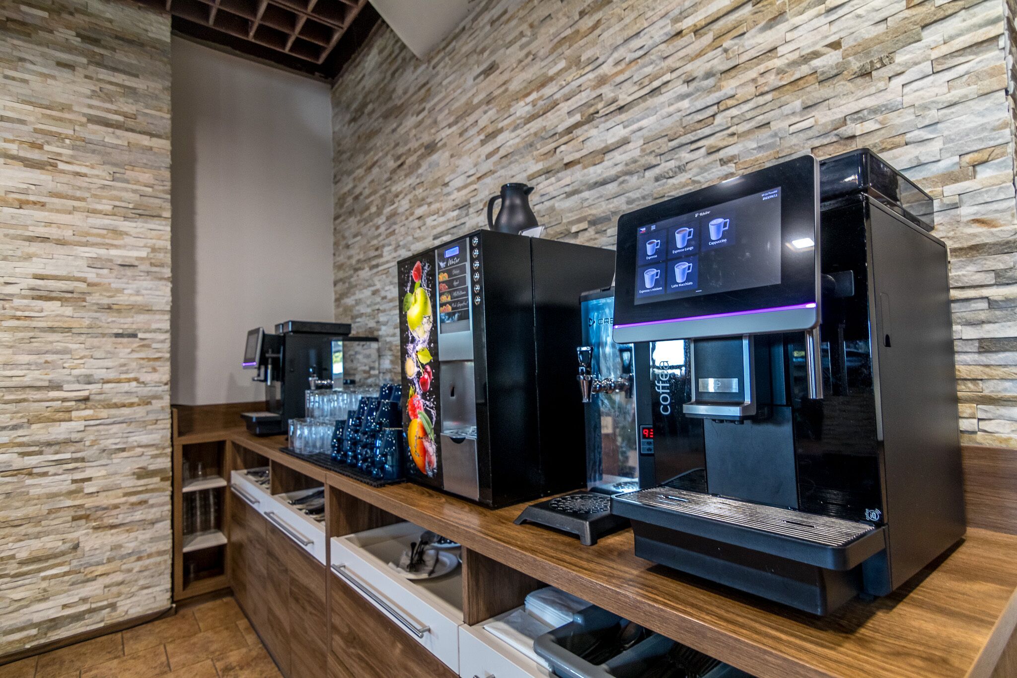A coffee station with multiple espresso machines and a coffee dispenser, set against a stone wall backdrop.