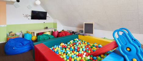 Una sala de juegos con una piscina de pelotas, un tobogán y un sillón de saco.