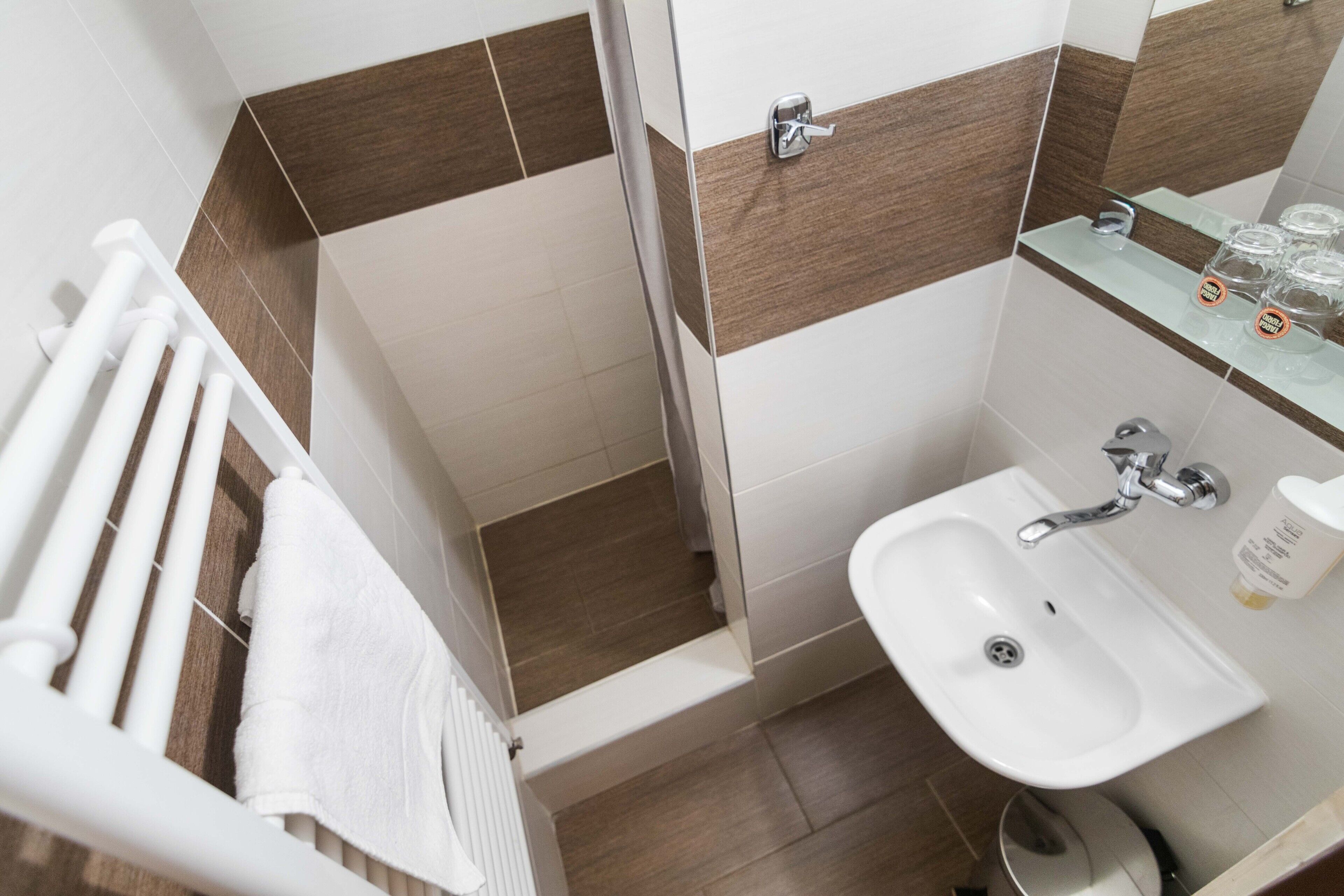 Un baño con lavamanos blanco, repisas de vidrio con artículos de aseo, y un perchero para toallas.