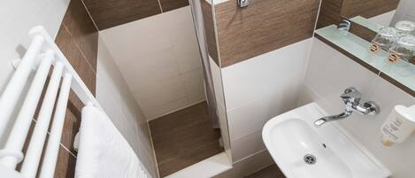 Un baño con lavamanos blanco, repisas de vidrio con artículos de aseo, y un perchero para toallas.