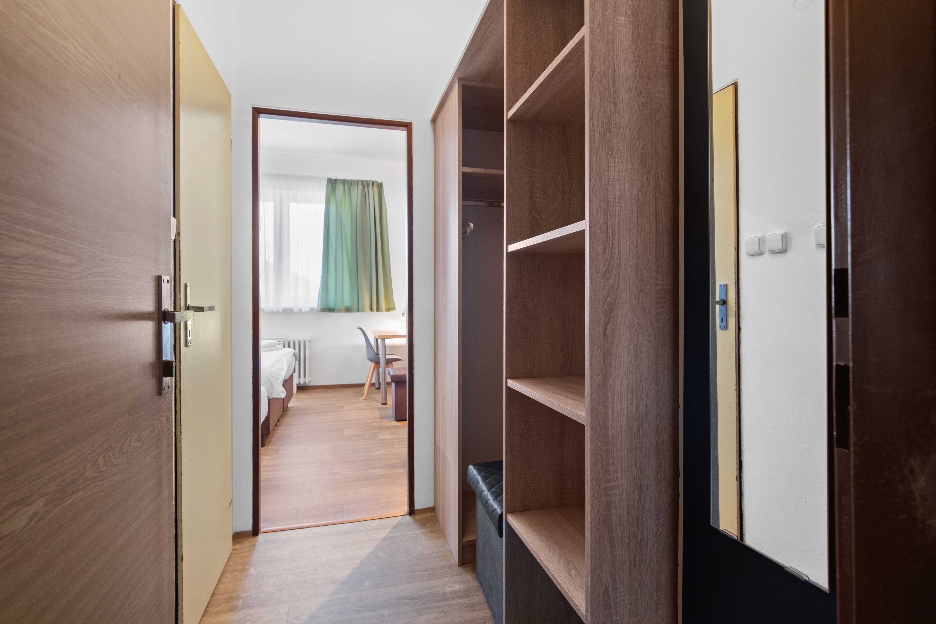 Un pasillo que conduce a un dormitorio con un armario de madera, un banco y vistas a un comedor con mesa y sillas.