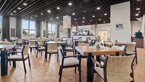 A spacious dining area with multiple tables and chairs, a kitchen in the background, and large windows allowing natural light. - Hotel Červenohorské sedlo (Loucna nad Desnou)