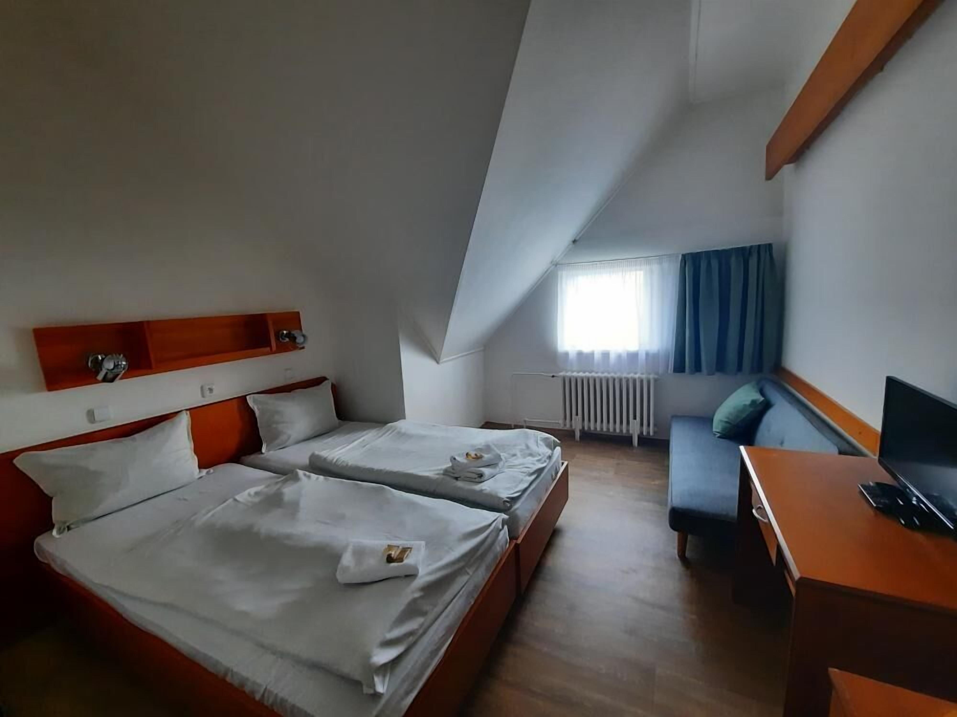 A hotel room with two beds, a desk, a TV, and a window with curtains.