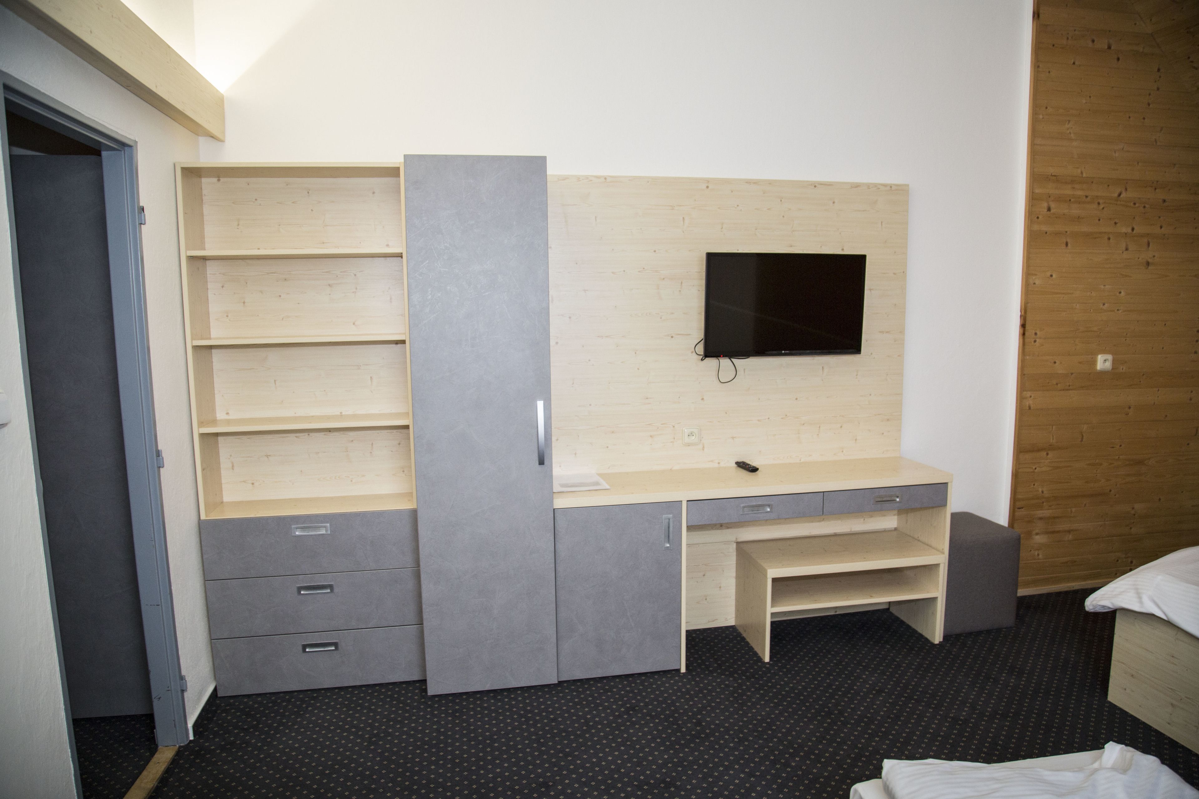 A room with a built-in desk, a flat-screen TV mounted on the wall, and a bed with a wooden headboard.