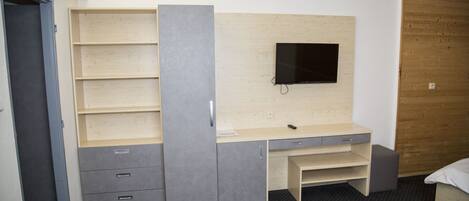 A room with a built-in desk, a flat-screen TV mounted on the wall, and a bed with a wooden headboard.