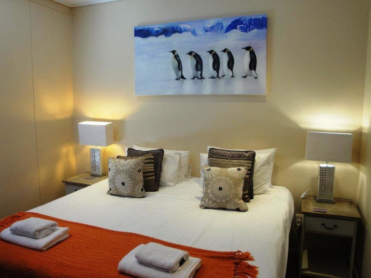 A hotel room with a bed, pillows, a blanket, a painting of penguins, and two bedside lamps.