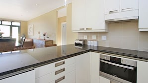 A modern kitchen with white cabinets, a built-in oven, and a countertop with a toaster. - Atlantic Views 6 (Cape Town)
